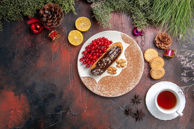 暗いテーブルの上のお茶とベリーとおいしいチョコエクレアの上面図甘いケーキパイデザート
