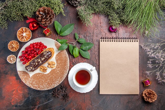 Вид сверху вкусные шоколадные эклеры с чаем и ягодами на темном столе, сладкие пирожные, пирог, десерт