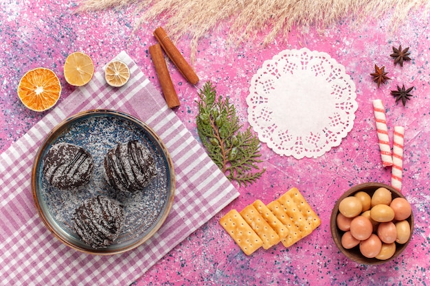 Top view yummy chocolate cakes with candies and crisps on a pink