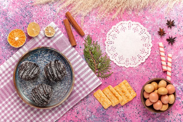 Top view yummy chocolate cakes with candies and crisps on a pink