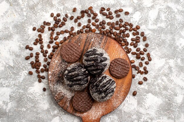 Top view of yummy chocolate cakes with cookies and brown coffee seeds on white surface