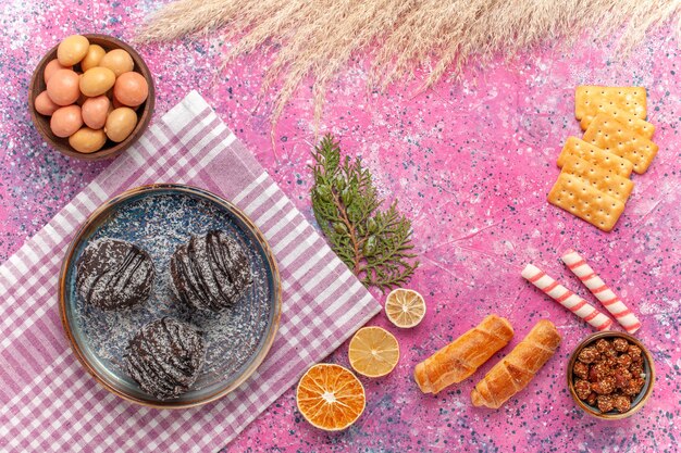 Top view yummy chocolate cakes with crackers and candies on pink