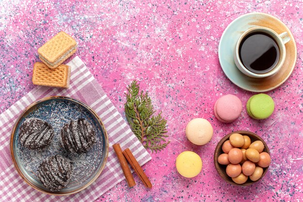 Top view yummy chocolate cakes with cup of tea and macarons on pink