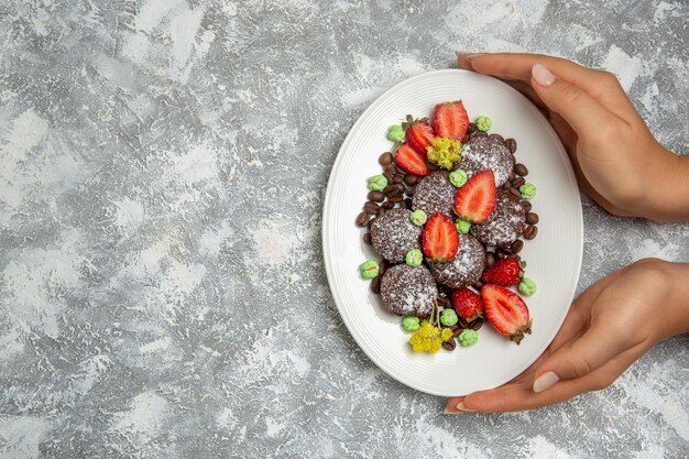 Вид сверху вкусные шоколадные торты со свежей красной клубникой и шоколадной стружкой на белой поверхности