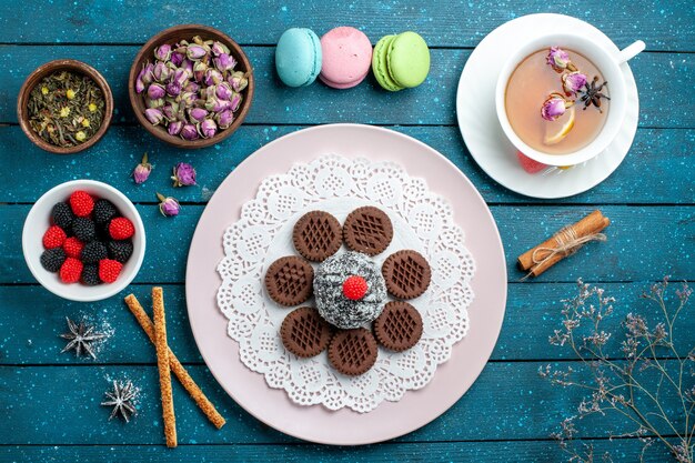 Вид сверху вкусного шоколадного печенья с конфитюрами и чаем на синем деревенском письменном столе, какао-чай, сладкое печенье
