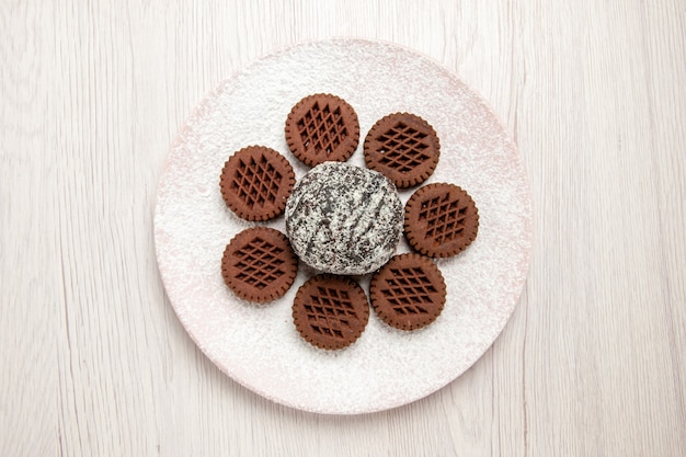 Vista dall'alto gustosi biscotti al cioccolato con piccola torta al cacao su bianco