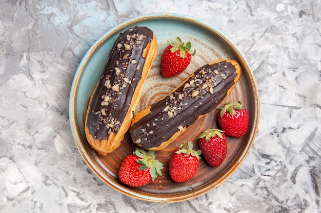 Вид сверху вкусные шоколадные эклеры с клубникой на легком фруктовом десертном торте