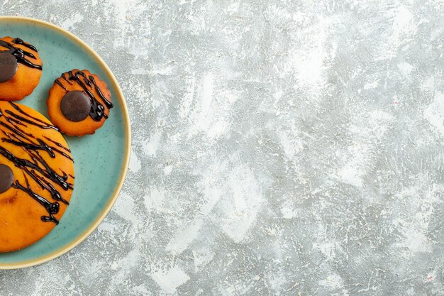 Top view yummy cocoa cakes with chocolate icing inside plate on a white floor cake biscuit dessert sweet cookie pie