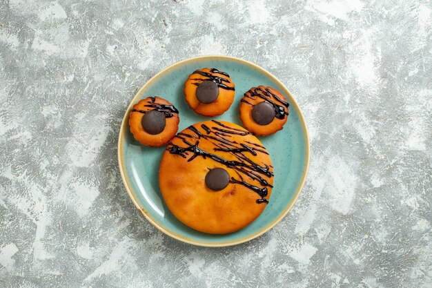 Top view yummy cocoa cakes with chocolate icing inside plate on a white surface cake biscuit dessert sweet cookie pie