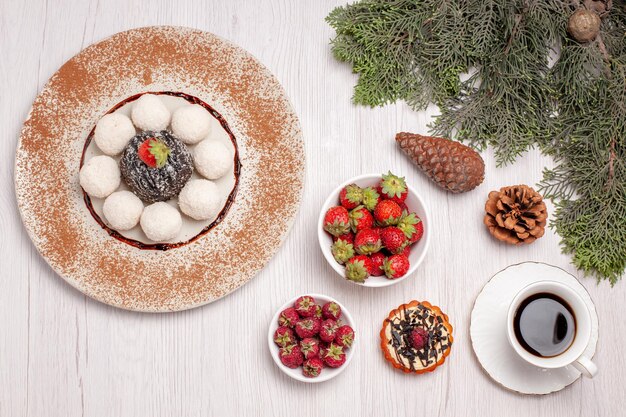 Top view of yummy coconut candies with cake tea and fruits on white