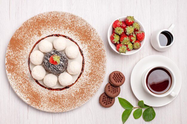 Top view of yummy coconut candies with chocolate cake and cup of tea on white