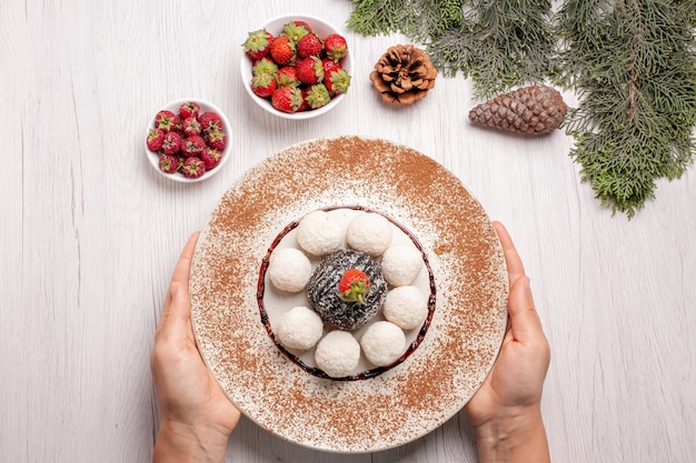 Vista dall'alto di deliziose caramelle al cocco con torta al cacao sul tavolo bianco