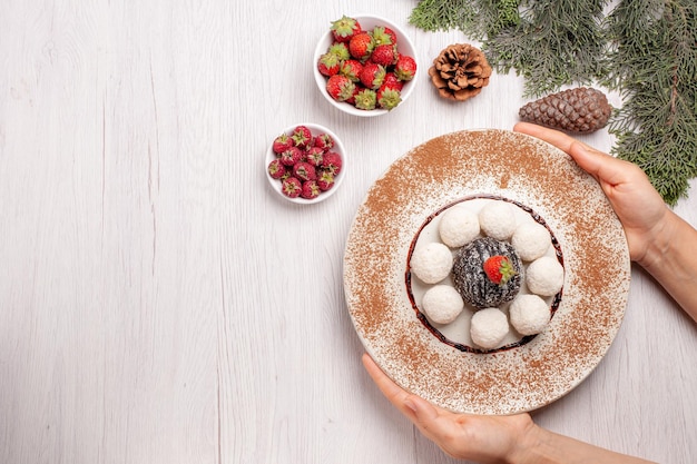 Top view of yummy coconut candies with cocoa cake on white