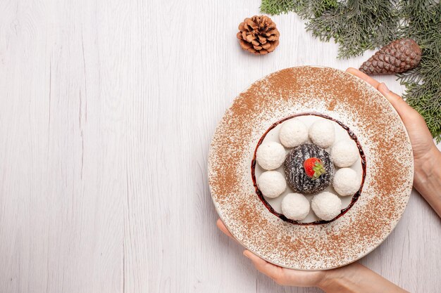 Top view of yummy coconut candies with cocoa cake on white