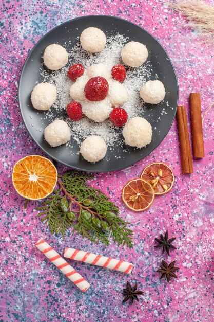 Top view of yummy coconut candies with fresh red strawberries on pink surface