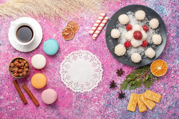 Top view of yummy coconut candies with macarons and cup of tea on the pink surface