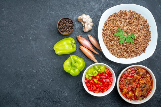 Вид сверху вкусной вареной гречки с овощами на темно-сером