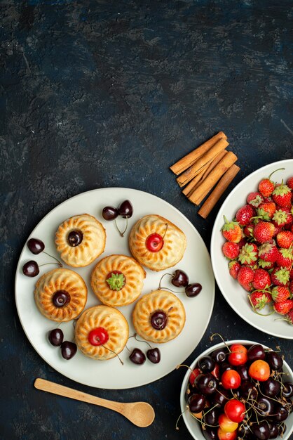 A top view yummy cookies inside white plate with cherries strawberries on the dark background fruit biscuit cake 