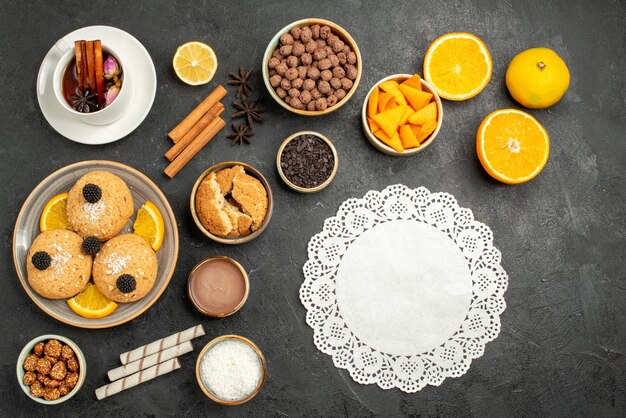Вид сверху вкусное печенье с чашкой чая и дольками апельсина на темном столе, торт, пирог, сахар, десерт, печенье