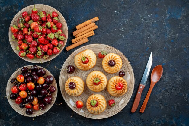 A top view yummy cookies with red strawberries cherries inside plate on the dark desk cookie 