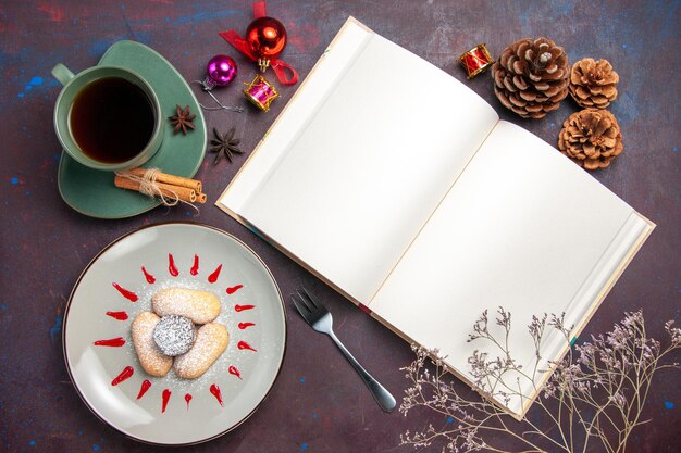 Free photo top view of yummy cookies with sugar powder and cup of tea on dark