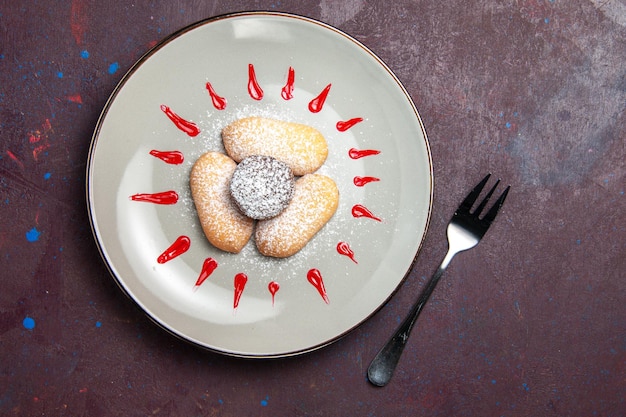 Вид сверху вкусного печенья с сахарной пудрой и красной глазурью внутри тарелки на черном