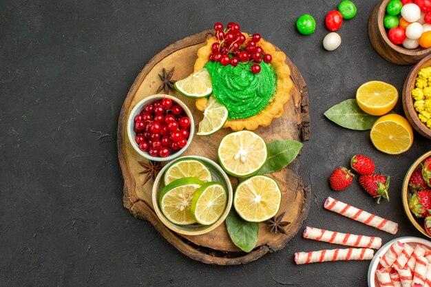 Top view yummy creamy cake with candies and fruits on dark background sweet cookie biscuits