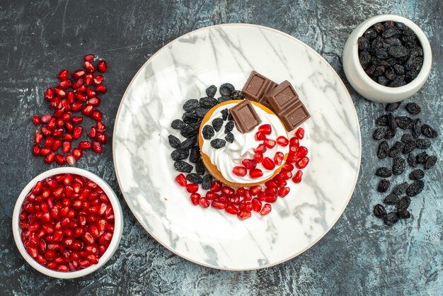 Top view yummy creamy cake with chocolate pomegranates and raisins on light-dark background