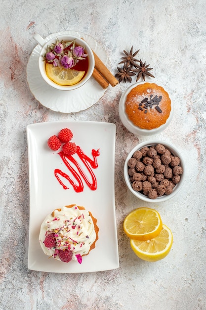 Foto gratuita vista dall'alto di una deliziosa torta cremosa con una tazza di tè e fette di limone su bianco