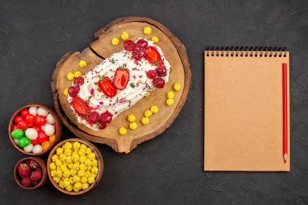 Top view of yummy creamy cake with fruits and candies on black floor biscuit tea cookie cake sweet candy