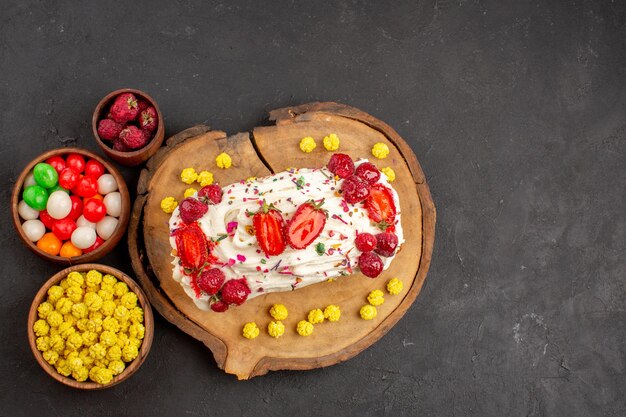 Top view of yummy creamy cake with fruits and candies on black