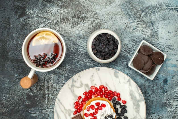 Foto gratuita vista dall'alto gustosa torta cremosa con uvetta e tazza di tè su sfondo chiaro-scuro