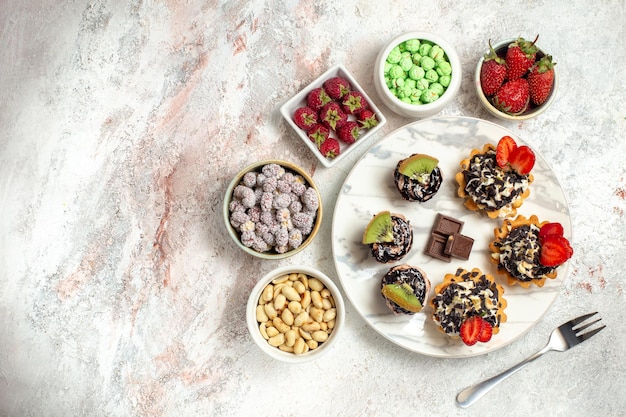 Foto gratuita vista dall'alto deliziose torte cremose con frutti di bosco e caramelle su superficie bianca biscotto torta alla frutta torta alla crema biscotti al tè