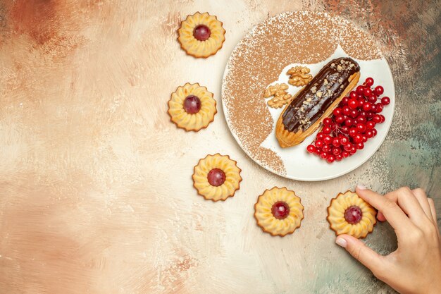 Top view yummy eclair with red berries and cookies on the light table cake dessert sweet