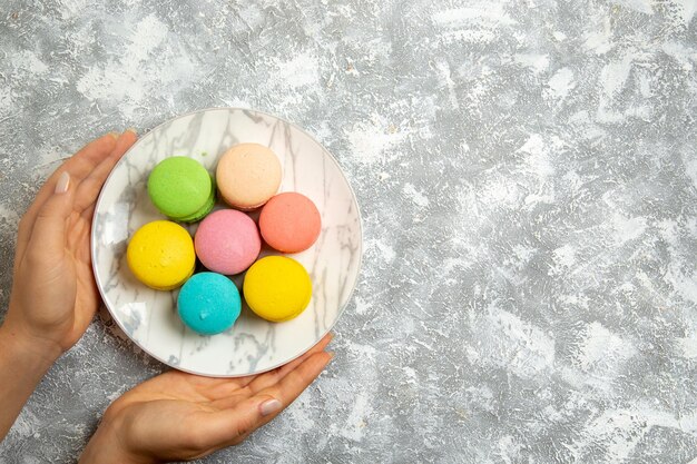 Top view yummy french macarons colorful cakes inside plate on white surface