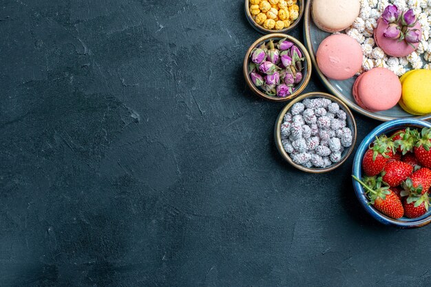 Top view yummy french macarons with candies and fruits on grey floor