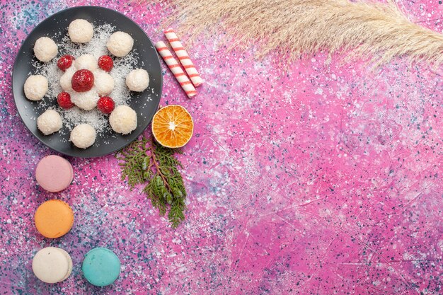 Top view of yummy french macarons with coconut candies on pink surface