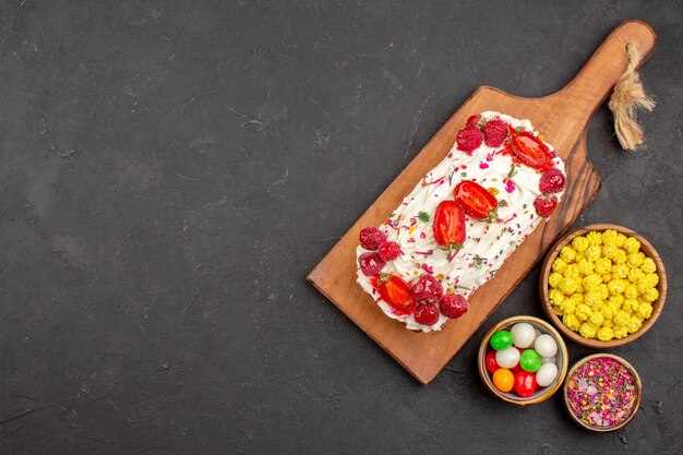 Top view of yummy fruit cake with candies on black