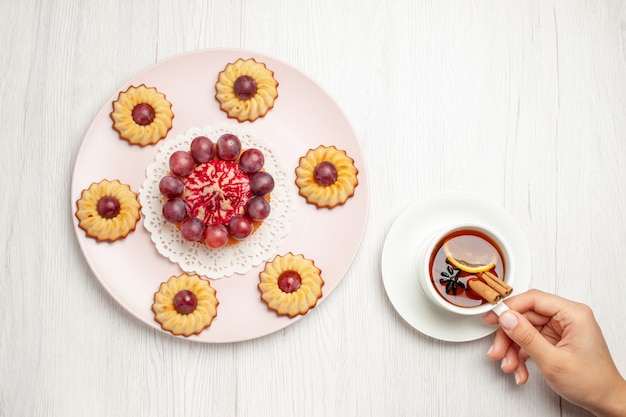 Top view yummy grape cakes with cup of tea on white table dessert biscuit pie cookie