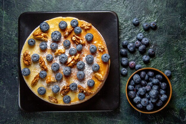 Top view yummy honey cake with blueberries and walnuts inside plate dark surface