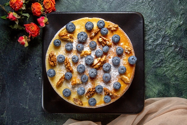 Вид сверху вкусный медовый торт с черникой и грецкими орехами внутри тарелки темной поверхности