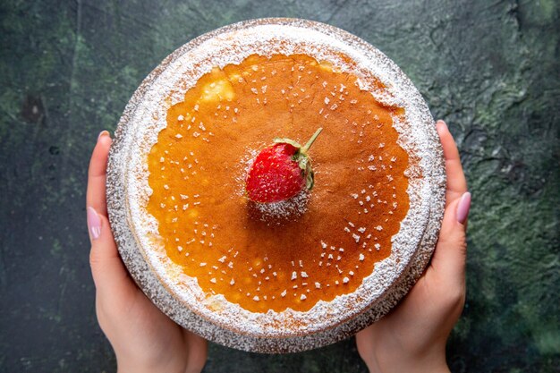 Вид сверху вкусный медовый торт с сахарной пудрой на круглой деревянной доске темной поверхности