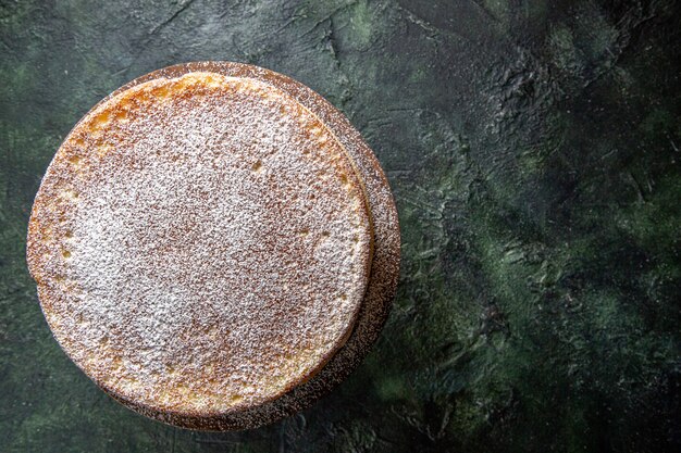 Top view yummy honey cake with sugar powder on round wooden board dark surface