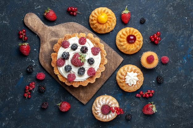 어두운 책상 베리 과일 케이크 비스킷 빵에 팔찌 쿠키와 함께 크림과 딸기가있는 맛있는 작은 케이크