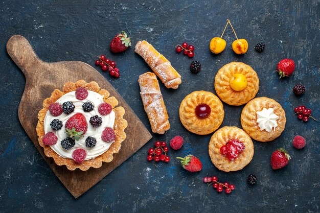 어두운 테이블 베리 과일 케이크 비스킷 빵에 팔찌 쿠키와 함께 크림과 딸기가있는 맛있는 작은 케이크