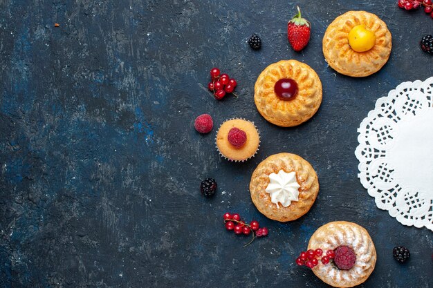 Вид сверху вкусные маленькие пирожные с ягодами фруктами на темном фоне ягодный фруктовый торт бисквит