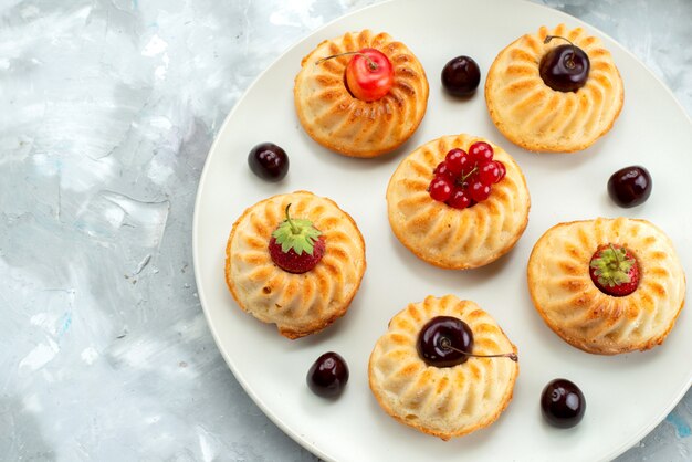 A top view yummy little cakes with berries and fruits inside plate cake biscuit sugar 