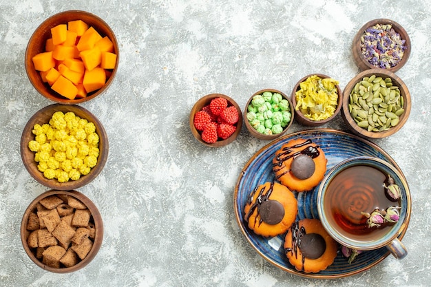 Top view yummy little cakes with candies and cup of tea on white surface cake biscuit cookie dessert sweet tea