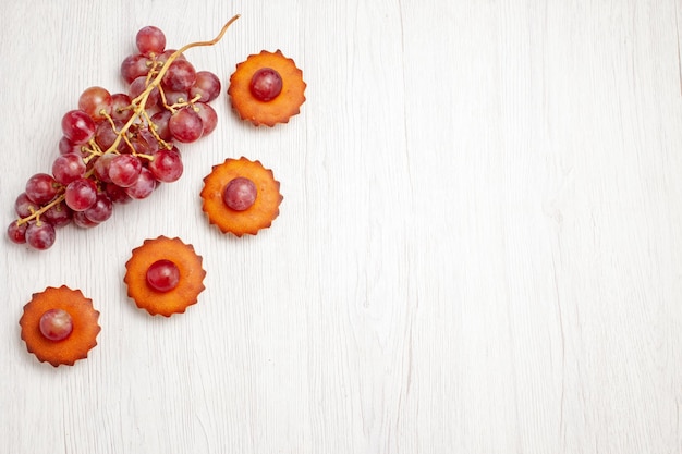 Top view yummy little cakes with fresh grapes on white surface dessert cookie biscuit tea cake pie