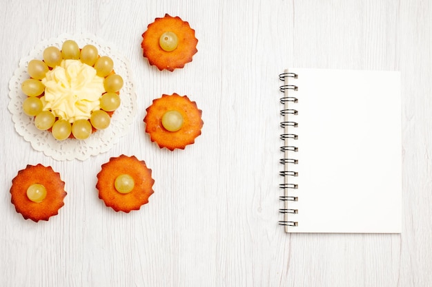 Top view yummy little cakes with green grapes on a white surface fruit tea dessert cookie biscuit cake pie